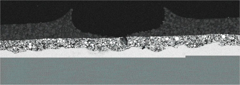 Fig. 1: Scanning electron microscope photo of a steel cross-section. The steel substrate is the shiny, smooth part toward the bottom—the granular, crystalline lighter gray layer is norganic zinc. The darker gray top layer is a high-solids epoxy, complete with a large burst bubble in the middle.